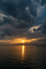 Obraz premium Dramatic sunset over Lake Constance seen from the Austrian shore in Bregenz, Vorarlberg, with the golden sun breaking through dark storm clouds and reflecting on the calm water surface