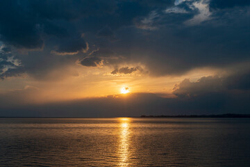 Obraz premium Dramatic sunset over Lake Constance seen from the Austrian shore in Bregenz, Vorarlberg, with the golden sun breaking through dark storm clouds and reflecting on the calm water surface