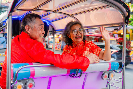 Couple enjoys ride in tuk-tuk while smiling and waving in busy city at night