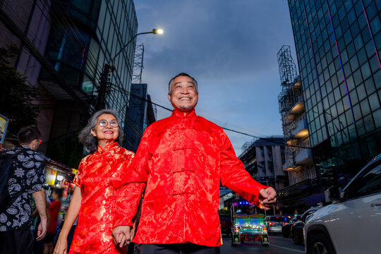 Couple walks hand in hand wearing red outfits during a festive night in a busy city street