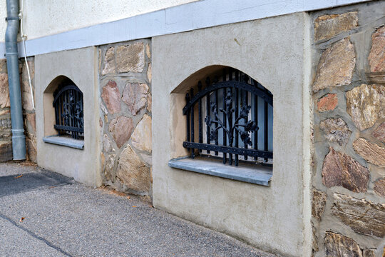 Basement windows with decorative wrought iron grilles on stone wall foundation