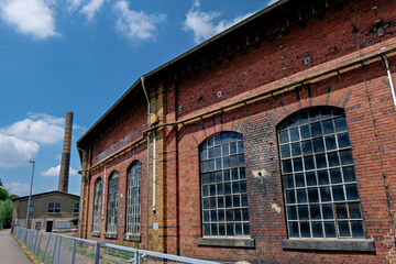 Obraz premium Old brick factory building with tall industrial chimney under blue sky