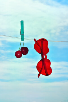Red cherries and sunglasses hanging on clothespin against a blue sky