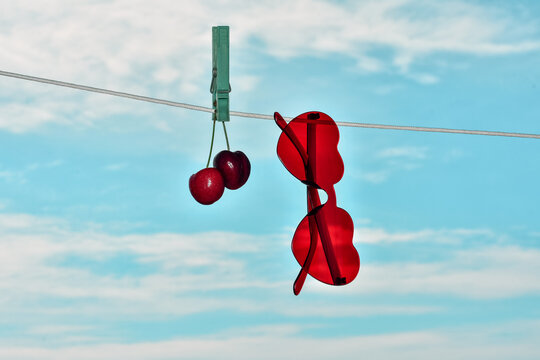 Red cherries and heart-shaped sunglasses hanging on clothespin