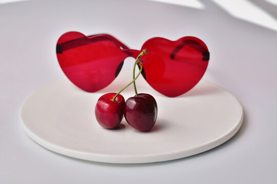 A pair of cherries in front of red heart-shaped sunglasses, love concept background