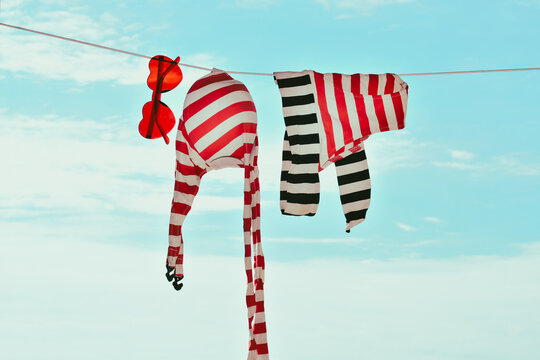 Retro red and white striped bathing suit and heart-shaped sunglasses hanging on clothesline against a blue sky