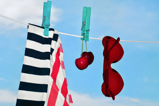 Swimsuit, cherries and red heart-shaped sunglasses hanging on a clothesline against a blue sky