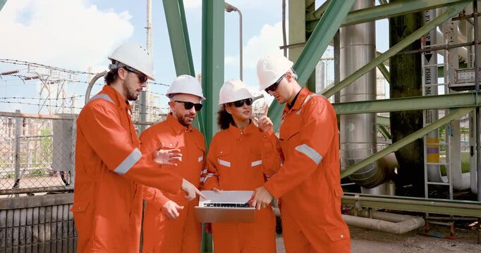 Multiracial refinery team discusses laptop data under pipe rack, planning safety inspection, maintenance checklist, compliance audit, hazard control for petrochemical operation onsite duty role.