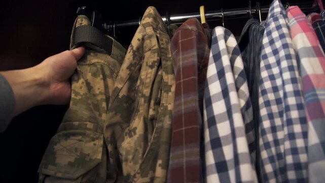 A man reaches for his military camouflage uniform hanging in a wardrobe