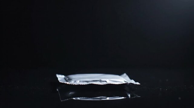 Close-up of a Single Silver Foil Sachet on Reflective Black Background