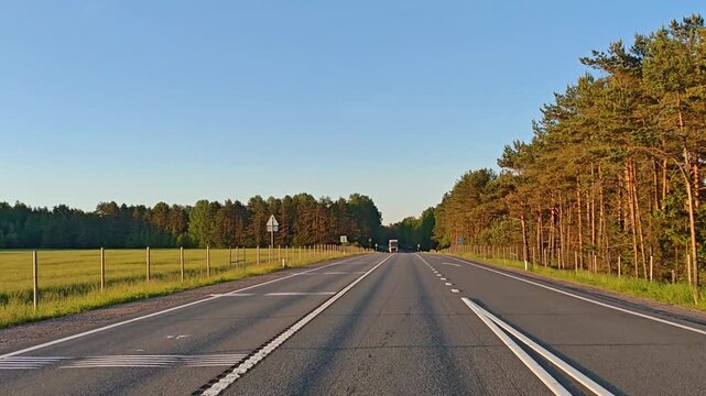 View through car windshield on a summer highway road with an oncoming truck, warm sunset sky with golden and orange tones, road trip driving perspective, travel and transportation scene