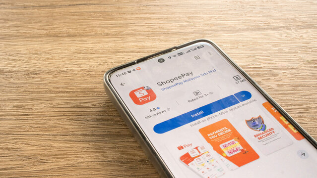 KULIM,MALAYSIA - JULY 13TH,2026 : A smartphone resting on a wooden desk showing the ShopeePay e-wallet and digital payment application download screen on the Google Play Store.