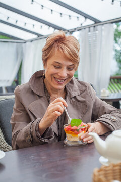 Smiling senior woman eating dessert while sitting in city street cafe