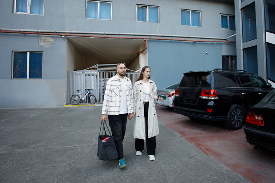 Couple walks through parking lot with bags in city setting during daytime