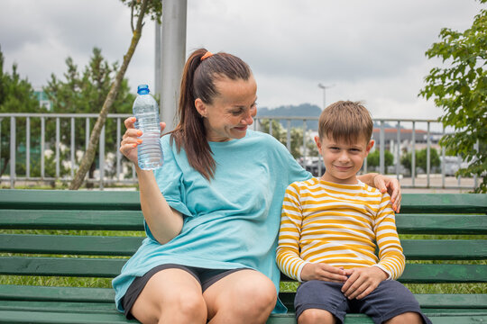 Healthy woman and child drinking pure water while resting on a bench in park after workout