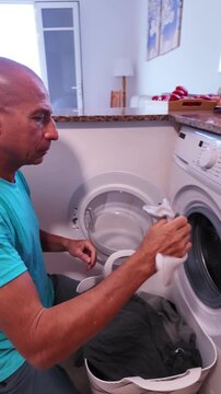 Daily domestic routine of a single man loading the washing machine with dark clothes from a laundry basket, then comically searching inside the drum for a missing sock