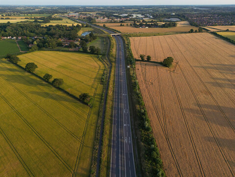 Aerial view of the Norwich Northern Distributor Road (NDR) running through agricultural fields near Norwich, Norfolk, England, during golden hour. British road infrastructure and English countryside