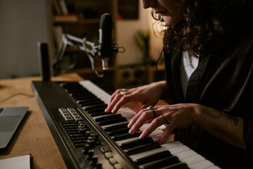 Close up of young adult musician playing keyboard at home studio, recording original rock music with microphone. Ideal for music production, home recording, creative career marketing © AnnaStills
