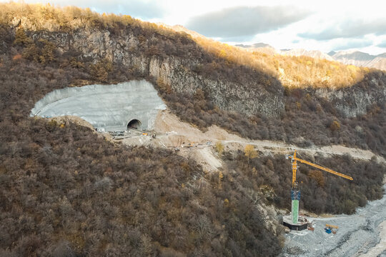 Aerial view of mountain tunnel construction with bridge infrastructure, Drone panorama of highway engineering project featuring excavation site crane and rugged mountain landscape