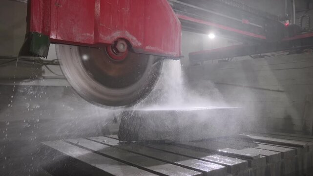 Industrial circular saw cutting a marble block in a factory with water cooling