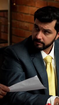 Working tirelessly on his laptop, frustrated Indian businessman overwhelmed with calls, paperwork, and deadlines while sitting at his corporate desk in cozy modern office with terracotta brick wall
