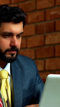 Working on laptop and thinking deeply, Indian businessman imagines future while gazing out of office window during break, wearing formal attire in cozy corporate workspace with terracotta brick wall