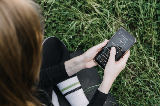 Hands hold smartphone displaying workout mix music playlist application against green grassy background. Fitness motivation, digital lifestyle, audio streaming, active living.