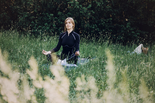 Woman meditating in a grassy field. Inner peace cultivation, serene outdoor meditation, wellness retreat imagery.