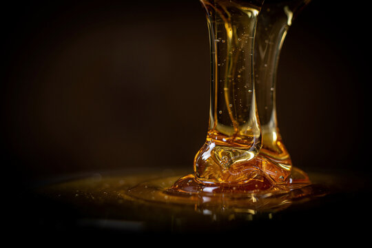 Golden honey pouring on dark background. Liquid syrup texture.