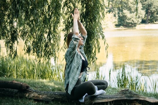 Woman meditating outdoors by lake, embracing natural energy, outdoor fitness and wellness, upward gaze meditation, sun salutation variation.