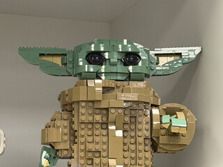 Obraz premium Brick-built baby yoda figure displayed on a shelf in a home interior, made from small building blocks and photographed close up.