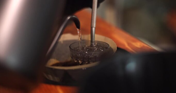 Gooseneck kettle pours hot water through a dispersion screen during pour over coffee brewing, detailed medium closeup, slow motion
