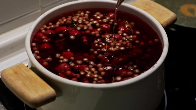 Wild strawberries and blackcurrants boiling in white ceramic pot on stove, homemade compote or jam cooking concept