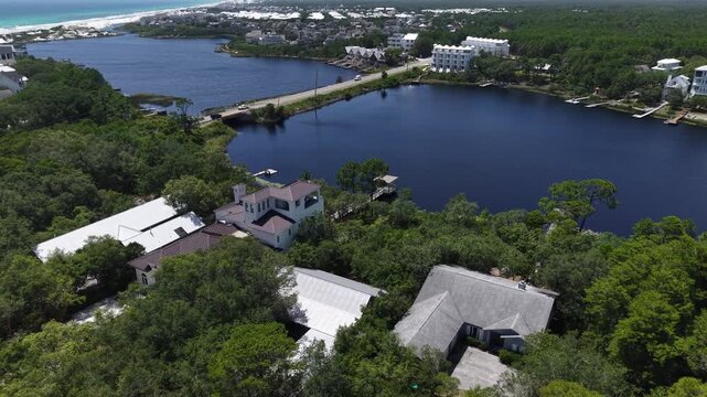 Aerial landscape about waterfront homes surrounding calm coastal Camp Creek Lake and forested areas with 30A Highway connecting two lakeshores, Florida, US