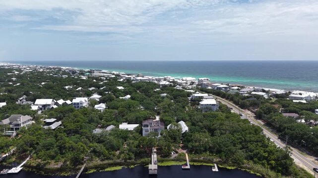 Backward tilted up drone fly of Camp Creek Lake luxury properties area near 30A Highway surrounded by lush coastal greenery and private docks with distant Gulf of Mexico landscape, Florida, US