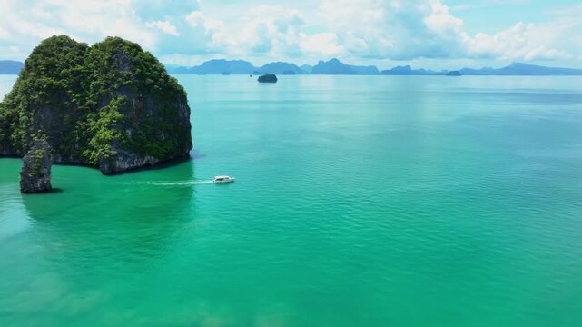 A small boat moves through turquoise waters near limestone karst formations in Ao Phang Nga National Park. Aerial tracking shot follows the vessel across calm tropical waters with distant islands.