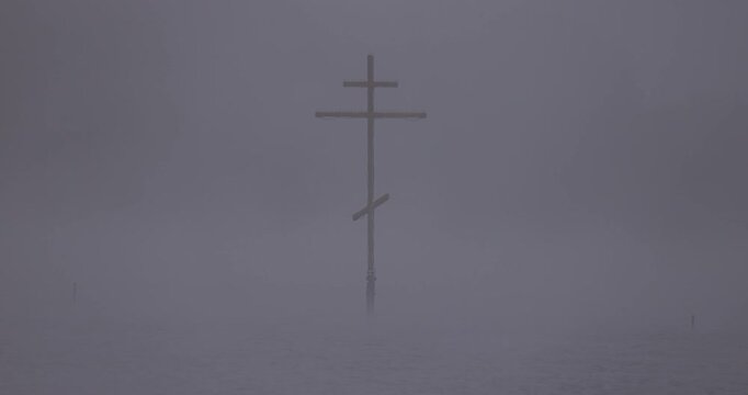 Close up view of an orthodox wooden cross standing in a lake in thick fog