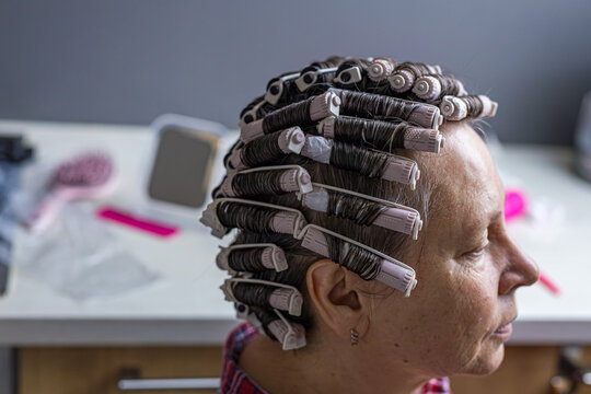 Woman wears perm rollers at home while waiting for a permanent wave to develop. DIY beauty routine represents self care, independence, and home hair transformation