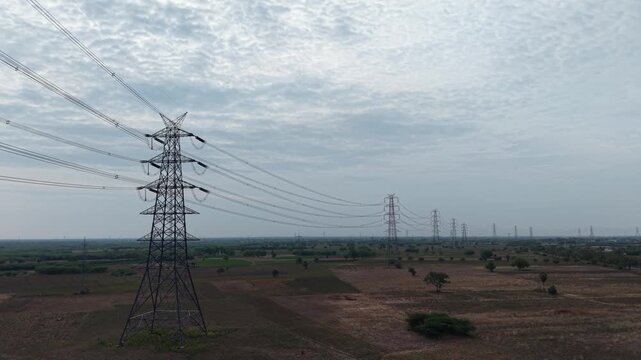 Power grid transmission tower and overhead cables spanning open dry farmland landscape