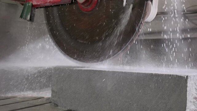 Industrial circular saw blade cutting granite block with water cooling in a stone processing factory