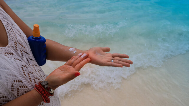 Woman hands applying sun protection lotion on the beach with turquoise sea background,Skin care and UV protection in summer concept