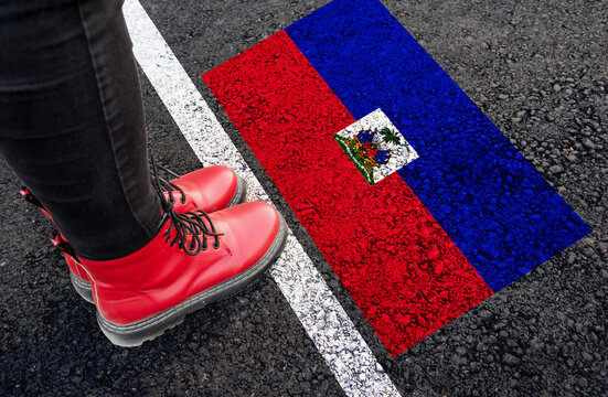 a woman with a boots standing on asphalt next to flag of Haiti and border
