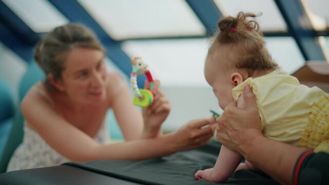 Baby engaging in a physical therapy session, improving motor skills and development with assistance from an adult and a rattle toy