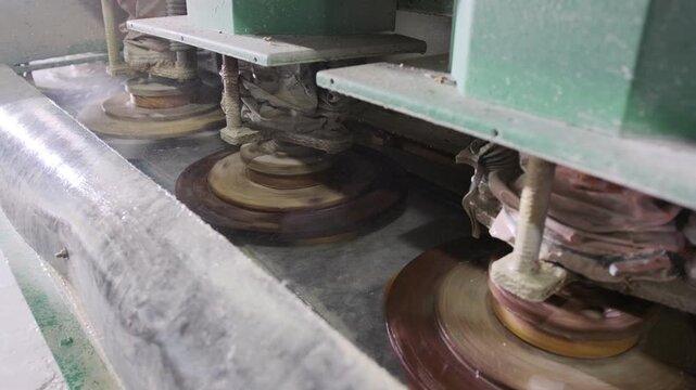 Industrial polishing machine grinding a marble slab with rotating abrasive heads in a stone processing factory