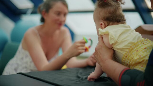 Mother and baby girl engaging in early intervention physical therapy. Therapist assisting child with motor skill development