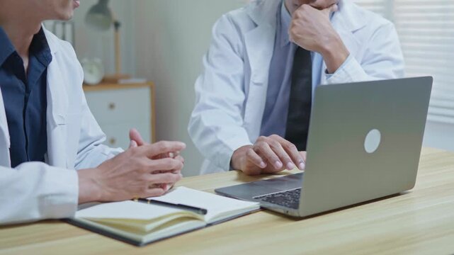 Doctors discussing a medical case together in a modern clinic office, using a tablet and laptop for telehealth, healthcare technology, medical consultation and health insurance planning.
