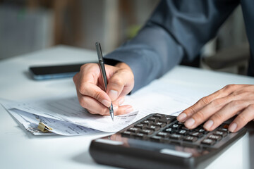 Fototapeta na wymiar Accountant hand using a calculator and writing on financial expense receipt documents at an office desk, representing tax calculation and auditing
