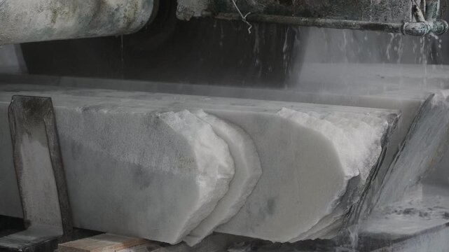 Industrial saw cutting a massive marble block with water cooling in a stone processing factory