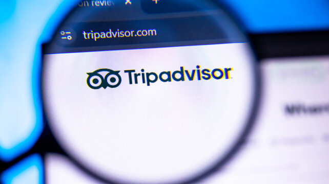 Tripadvisor logo on computer screen through magnifying glass.