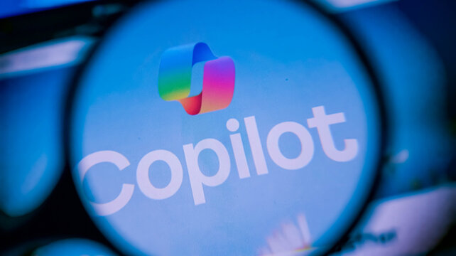 Magnifying glass focused on copilot logo on screen showing tech.